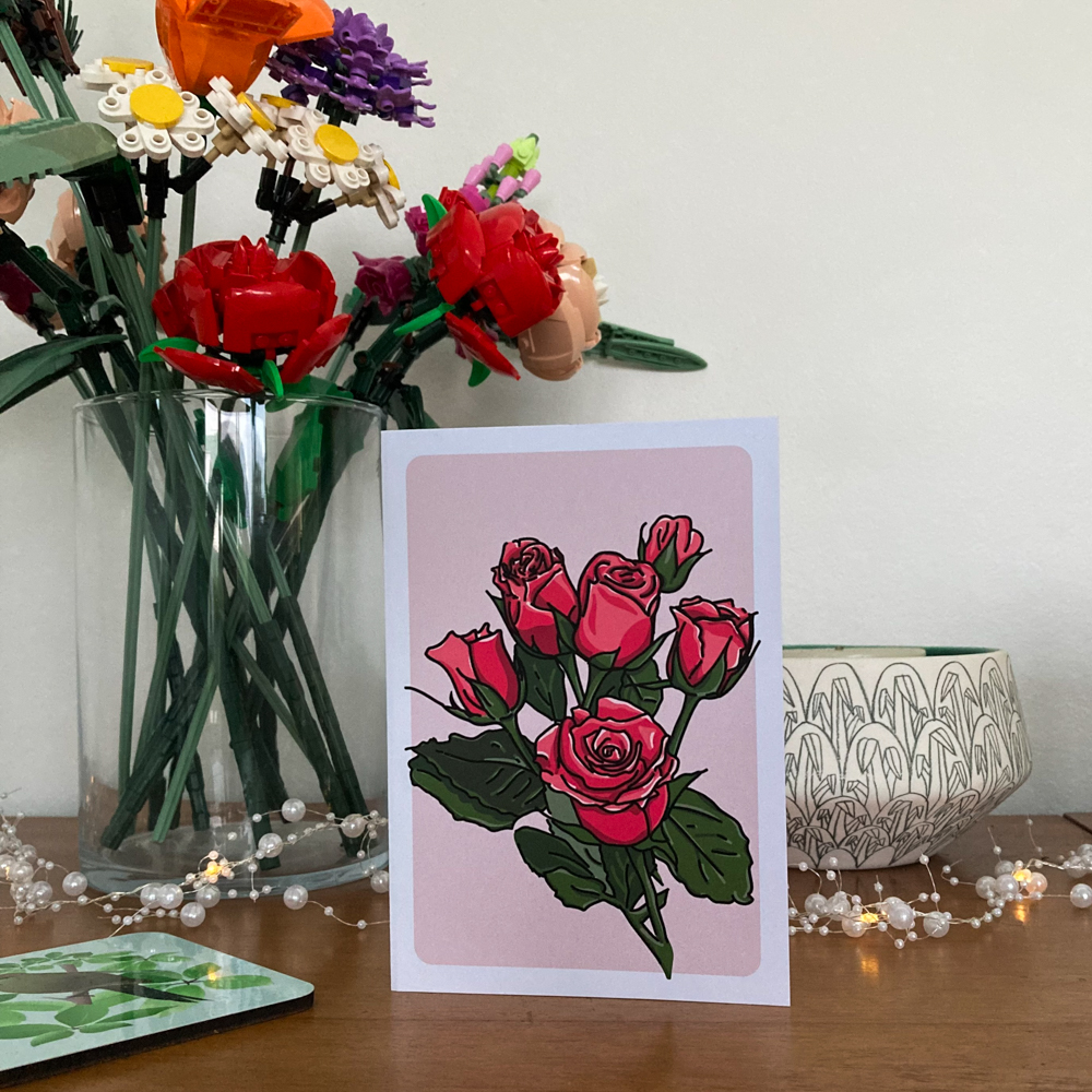 A greeting card featuring an illustration of pink roses sitting on a wooden sideboard amongst other decor items.